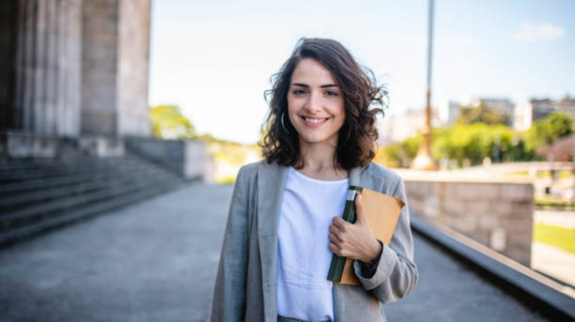 Close-up of relaxed female law student in casual attire standing with book at entrance to university in Buenos Aires.