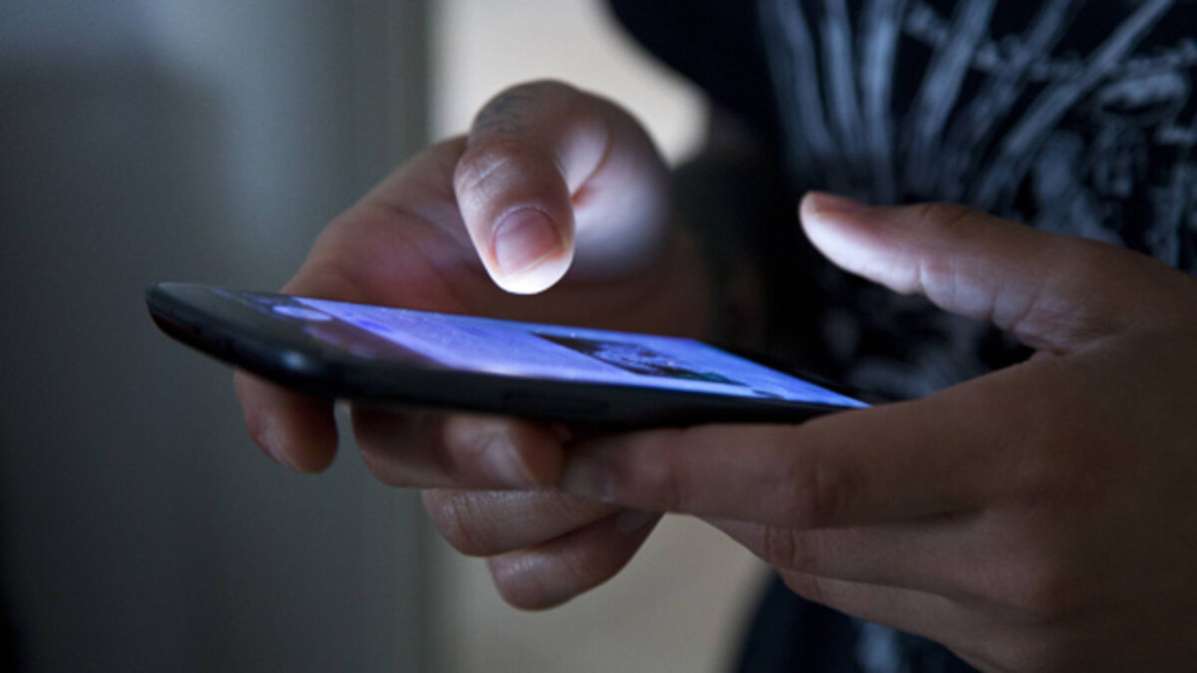 Hands holding smartphone in the dark.