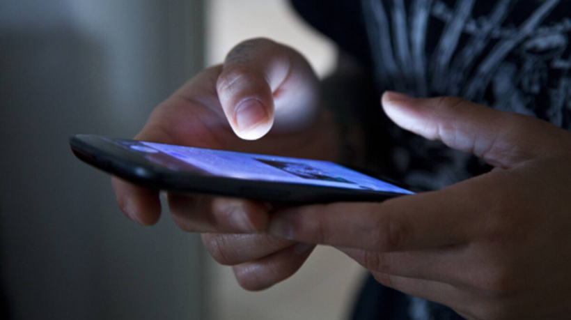Hands holding smartphone in the dark.
